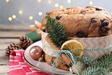 Tasty panettone cake with spices and Christmas decor on wooden table against grey background with blurred lights, closeup