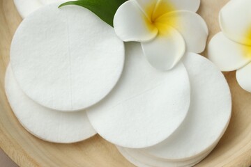 Clean cotton pads and plumeria flowers in wooden bowl, top view