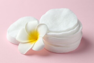 Clean cotton pads and plumeria flower on pink background, closeup