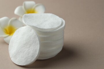 Stack of clean cotton pads and plumeria flowers on beige background, closeup. Space for text