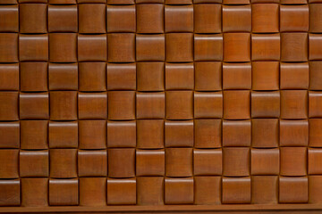 Full frame texture of a modern wooden wall panel. The geometric pattern of rounded, woven squares creates a luxurious and seamless background for interior design.