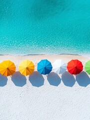 An aerial view shows a line of colorful beach umbrellas on a white sandy shore with the clear turquoise ocean lapping at the edge.