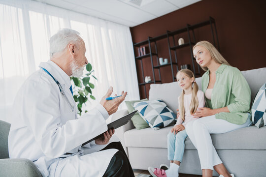 Funny friendly doctor chats with mom and daughter in a cozy home living room sharing health tips and care during a friendly checkup