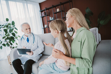 Obraz premium A warm family moment as a doctor speaks with mother and daughter in a cozy living room about health and care during a friendly home visit