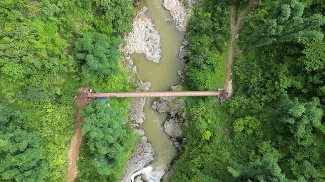 Aerial view of a wooden bridge spanning a flowing river surrounded by lush green forest, a scenic blend of nature's tranquility, Sa Pa, Lao Cai, Vietnam.