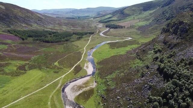Aerial view of a winding river flanked by a path cutting through a valley, showcasing contrasting greens and purples, Brechin, Scotland, United Kingdom.