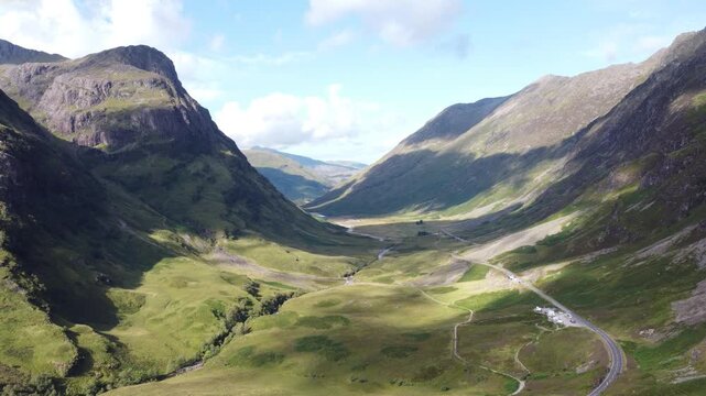 Aerial view of the majestic Glencoe mountains, their rugged peaks casting shadows on the lush green valley below, Glencoe, Scotland, United Kingdom.