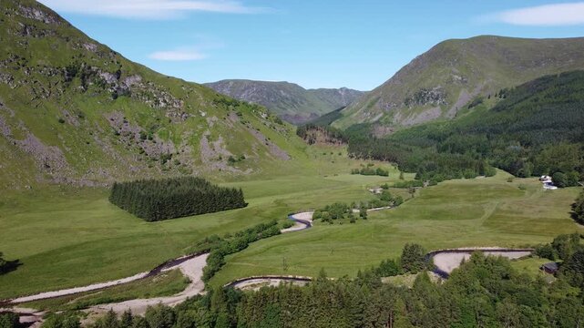Aerial view of lush green mountainsides descend into a vibrant valley, a river snakes through the landscape, Kirriemuir, Scotland, United Kingdom.