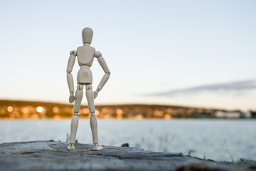 A wooden figure stands on a rock overlooking a body of water