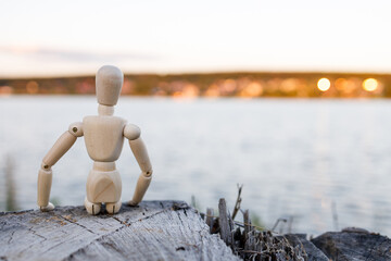 A wooden figure is sitting on a log by a body of water