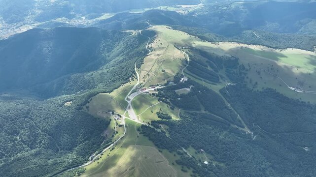 Aerial view of the Route des Cretes, a scenic road winding through lush green mountains and forests under a bright sky, Fellering, Grand Est, France.