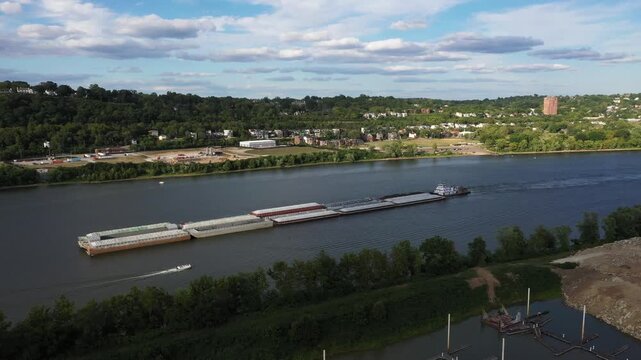Aerial view of a barge gliding on the tranquil Ohio River under a sunny sky, contrasting with the lush green banks, Cincinnati, Ohio, United States.
