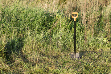 A black and orange shovel is standing in a field of tall grass