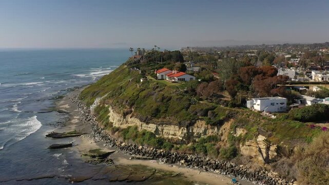 Aerial view of Yogananda Ashram atop a cliff, contrasted against the blue ocean and sky, with lush greenery cascading down to the rocky beach, Encinitas, California, United States.
