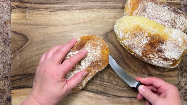 A freshly baked, delicious loaf of homemade ciabatta is cut lengthwise into two halves on a wooden board. Ciabatta on a walnut wooden cutting board.