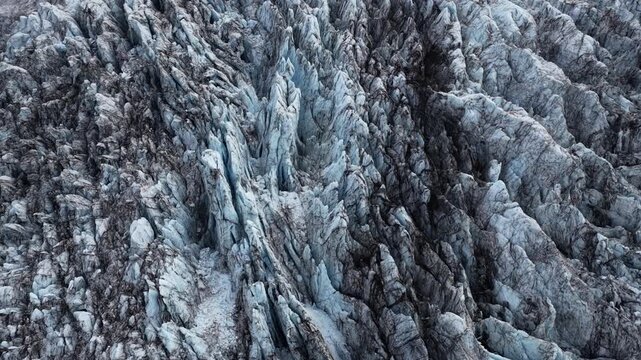 Aerial view of a glacier showing contrasting textures of blue ice and dark streaks creating a dramatic landscape, Sveitarfelagid Hornafjordur, Iceland.