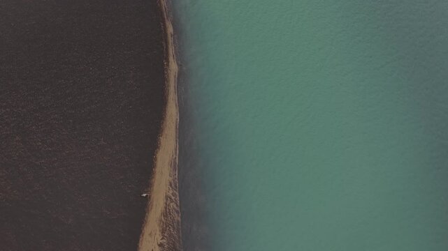 Aerial view of stark contrast of dark sand against the turquoise water, separated by a strip of land, creating a mesmerizing landscape, Iceland.