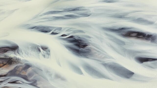 Aerial view of a glacial river creating stunning braided patterns, where pale water flows through darker sediment, creating a serene landscape, Iceland.
