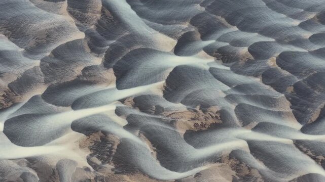 Aerial view of the glacial river carves a mesmerizing landscape of braided patterns, contrasting dark sediment against pale water, Iceland.