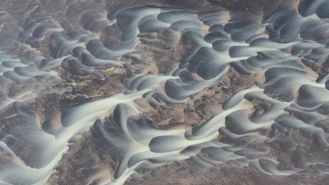Aerial view of glacial rivers creating intricate patterns across the landscape, showcasing the stark contrast between the dark earth and white water, Iceland.