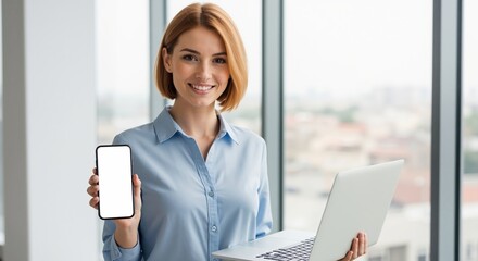 Confident businesswoman holding a laptop and showing a smartphone with a blank white screen. Professional woman in a modern office presenting a mobile device for mockup