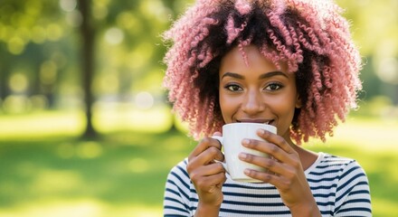 Smiling Black woman with pink curly hair drinking coffee in a park. Happy young African American female enjoying a hot beverage outdoors with copy space