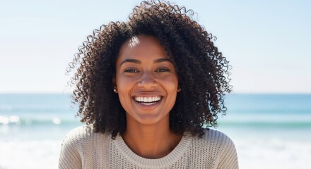Happy young African American woman with curly hair smiling at the beach. Close-up portrait of a cheerful female enjoying a sunny day outdoors by the ocean