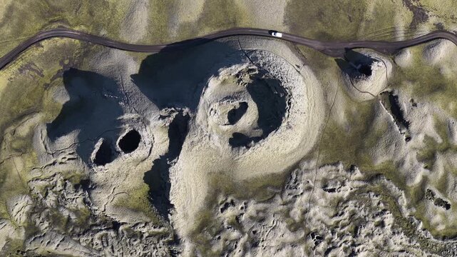 Aerial view of volcanic craters and a road cutting through the stark landscape, creating a textured scene of light and shadow, Laki volcano, Skaftarhreppur, Iceland.