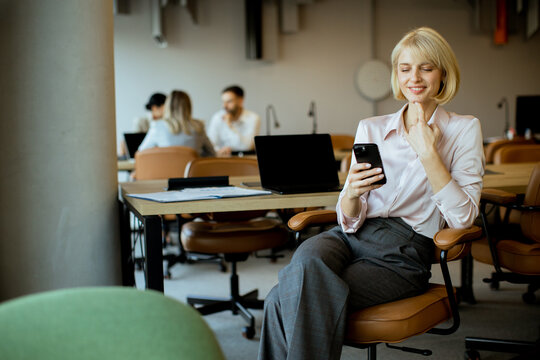 Young woman using smartphone while sitting in modern office workspace