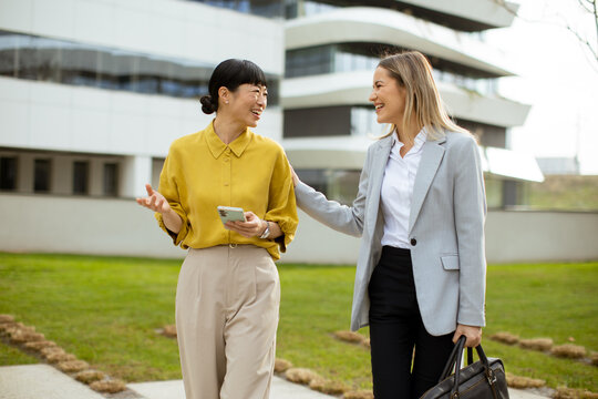 Two friends chatting and walking outside a modern building on a sunny day - Powered by Adobe