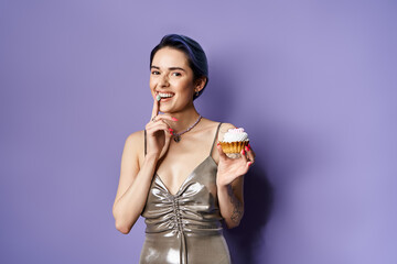 Stylish young woman with cupcake poses playfully against a vibrant purple backdrop