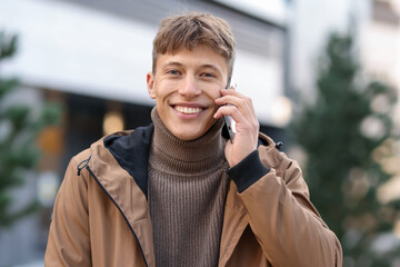 Portrait of smiling man in jacket talking by smartphone on city street