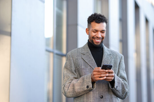 Smiling man in suit with smartphone on city street. Space for text