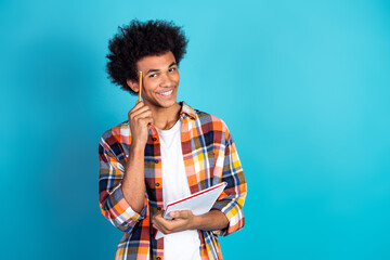 Young man with pencil and notebook smiling against blue background showcasing casual student style and creative learning vibe