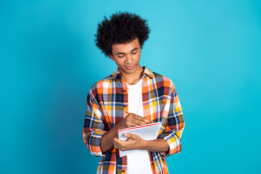 Young man student writing in notebook against blue background showcasing casual fashion and study focus - Powered by Adobe