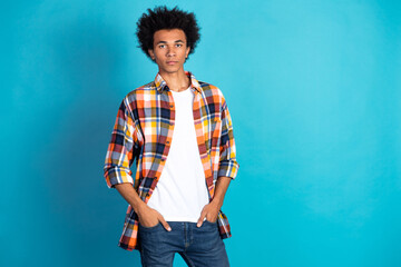 Young man in colorful plaid shirt white tee and blue jeans poses against blue background showcasing casual fashion style and confident lifestyle vibe