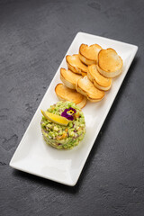 Avocado tartare with toasted baguette slices on white plate, gourmet appetizer