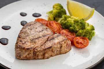 Grilled tuna steak with broccoli, cherry tomatoes and lemon on a white plate