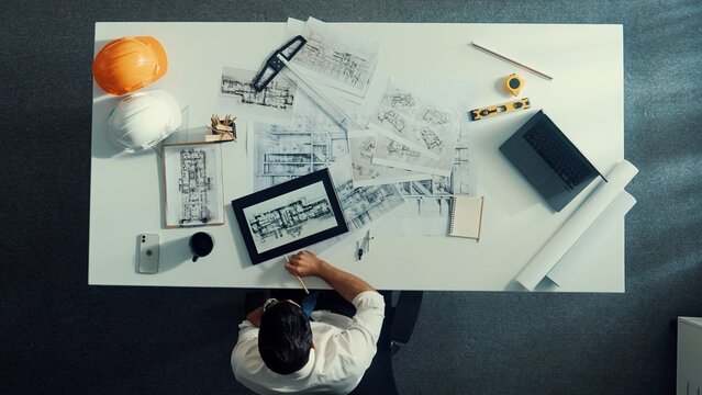Top down view of engineer looking at tablet while checking building material at paper or document. Aerial view of skilled architect design house construction while looking at blueprint. Alimentation.