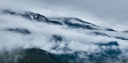 Misty Mountain Ridge Shrouded in Clouds Over Snow-Capped Peaks in BC, Canada