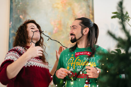 A couple in festive sweaters plays with holiday lights, sharing a joyful moment during the festive season. - Powered by Adobe