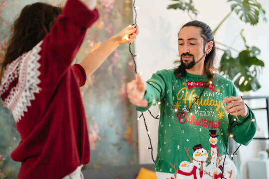 A man and woman decorate for the holidays, holding a string of festive lights.