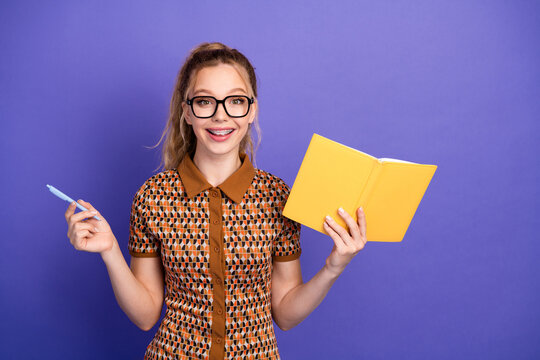 Young girl student with glasses smiles holding a yellow notebook and pen against a purple background for education fashion lifestyle stock photo
