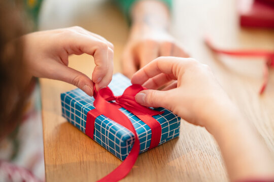 Hands carefully tie a red ribbon around a blue gift box, preparing a present for someone special.