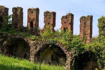 Fototapeta premium brick wall of a medieval castle with arches and characteristic battlements, partly covered by vegetation