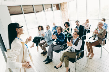 Professional speaker engages audience during business training seminar in bright conference room with diverse coworkers