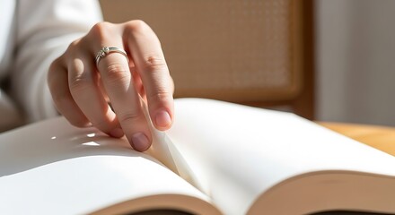 Closeup of a persons hand with a ring gently turning a page of an open book, bathed in warm natural light indoors