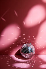 Shiny disco ball, also known as mirror ball, on a pink surface with scattered light reflections.