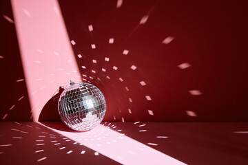 Shiny disco ball, also known as mirror ball, on a pink surface with scattered light reflections.
