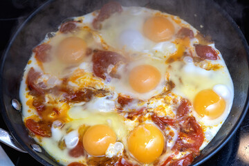 Fresh eggs frying with tomatoes.